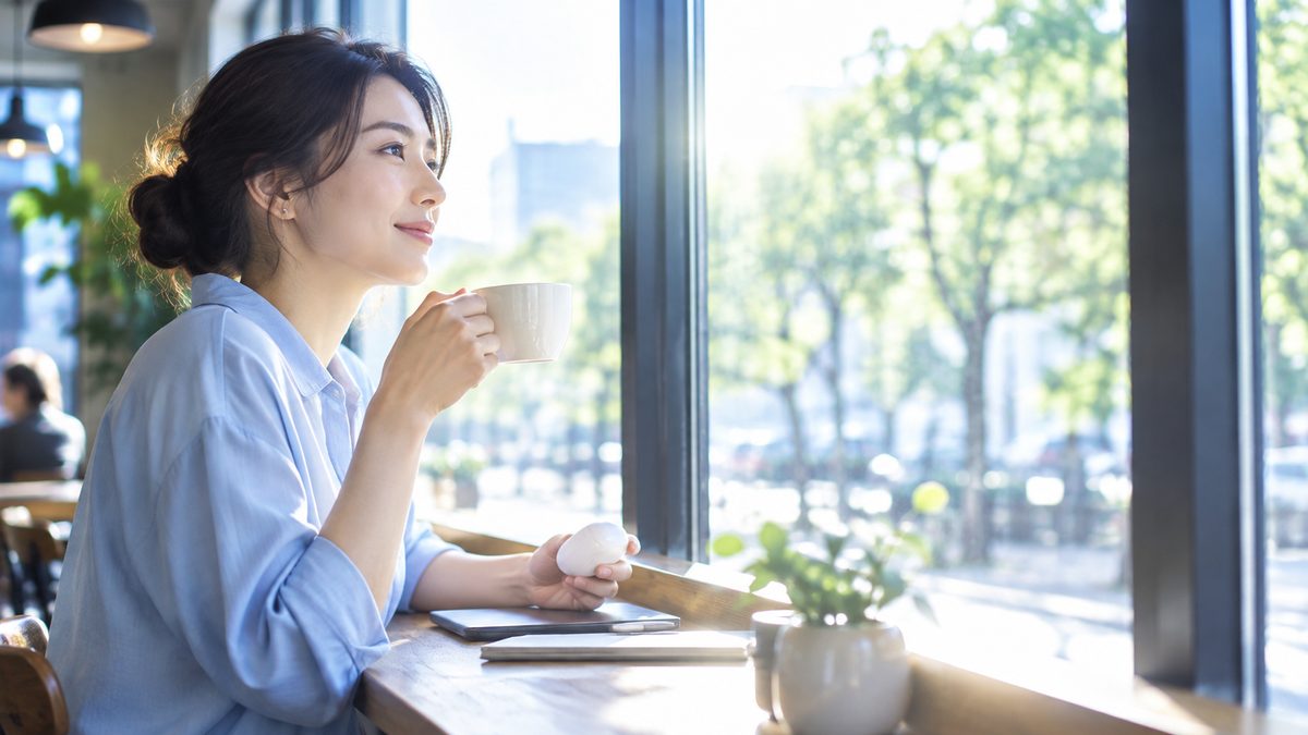 英語ニュースが聞き取れない悩みの疑問を整理しながら、カフェの窓際でイヤホンを手に次の学習を考える女性